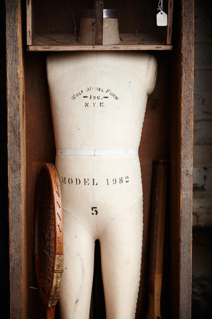 Vintage mannequin torso stands in a wooden cabinet, featuring a tennis racket and subtle studio lighting, creating an artistic composition.