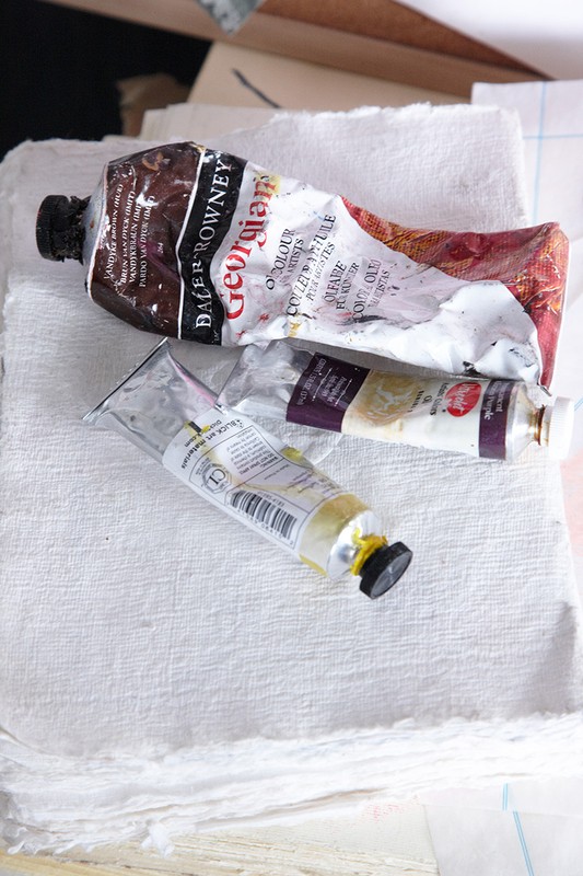 Two tubes of artist's paint laying on top of a stack of textured white paper in a close-up studio shot.