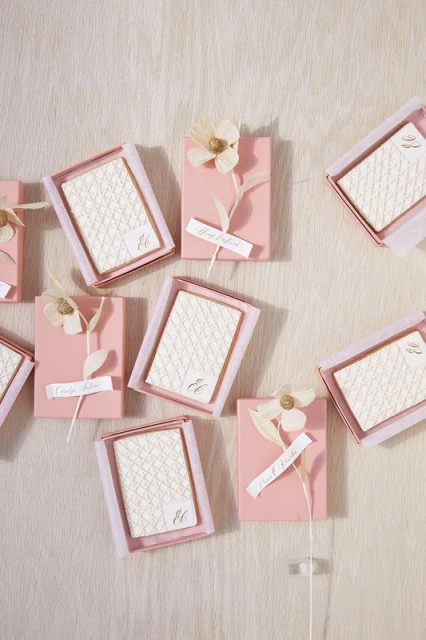 Arrangement of pink favor boxes with ivory-toned accents, floral decorations, and custom name tags displayed on a textured surface.