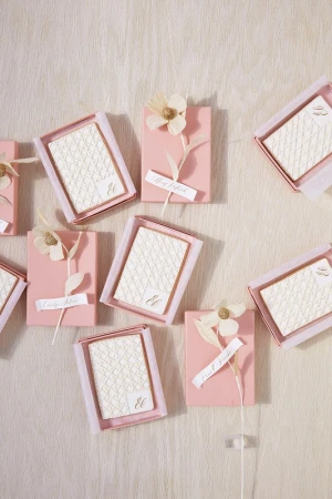 Arrangement of pink favor boxes with ivory-toned accents, floral decorations, and custom name tags displayed on a textured surface.