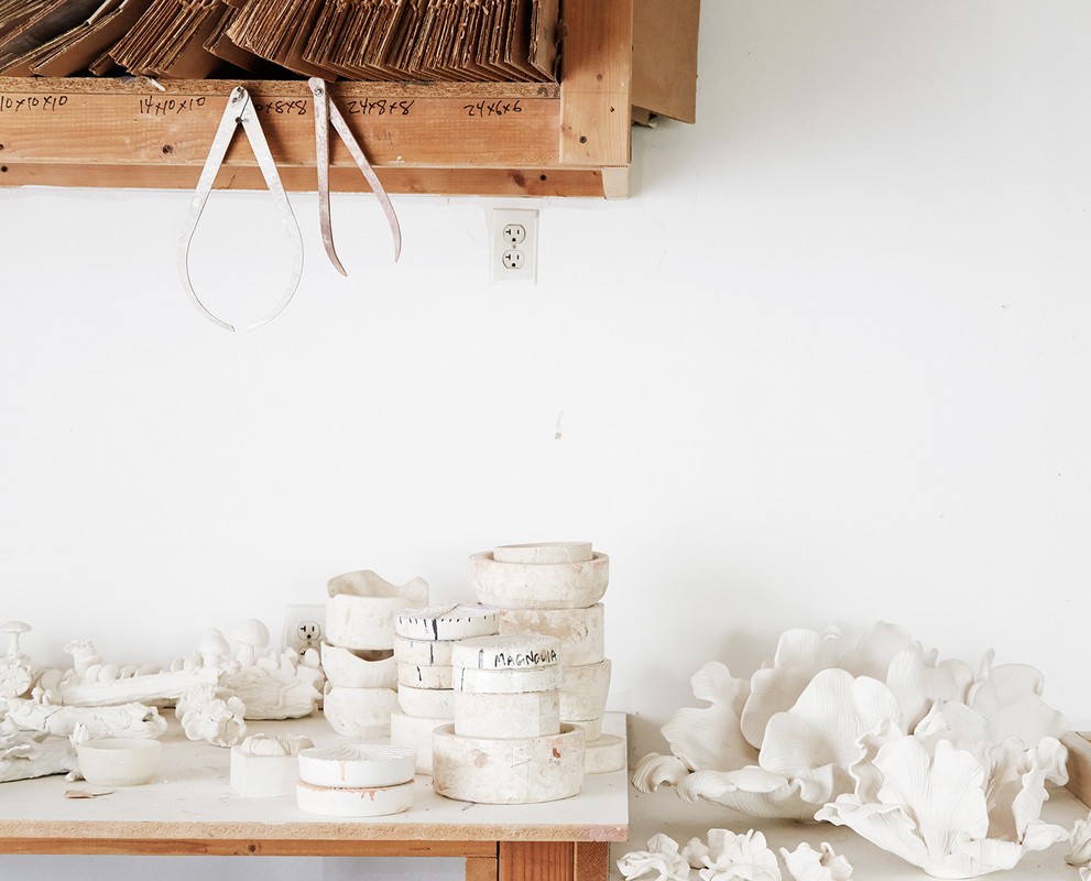 Still life of handmade ceramic bowls and art tools on a wooden table in a white-walled studio, emphasizing craftsmanship and art creation.