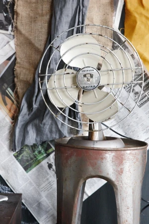 Vintage Emerson Electric fan on a metal stand is displayed in front of newspaper and fabric scraps in a studio setting. 