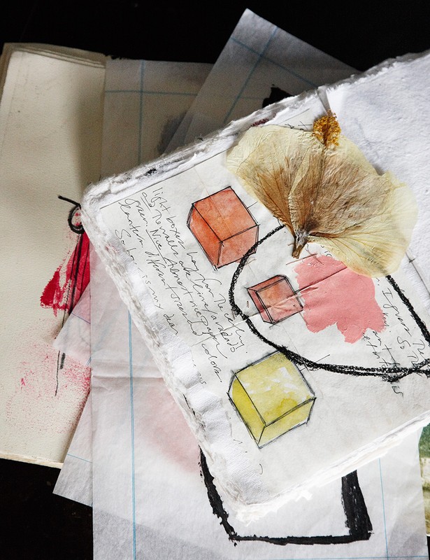 Open sketchbook with colorful cube drawings, pressed flower, and handwriting on textured paper, creating an artistic, layered still life.