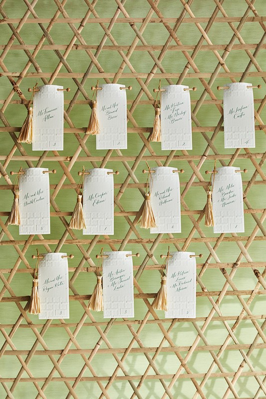 Wedding seating chart on a wooden lattice with small cards featuring guest names and gold tassels. Elegant reception decor.
