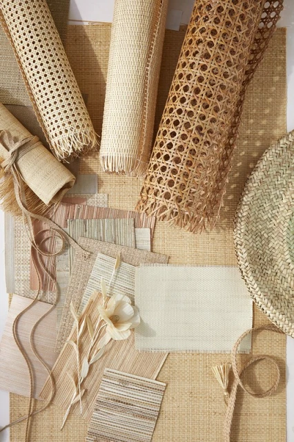 Overhead shot showcases an assortment of woven cane webbing rolls, textile samples, and a woven basket on a light surface.