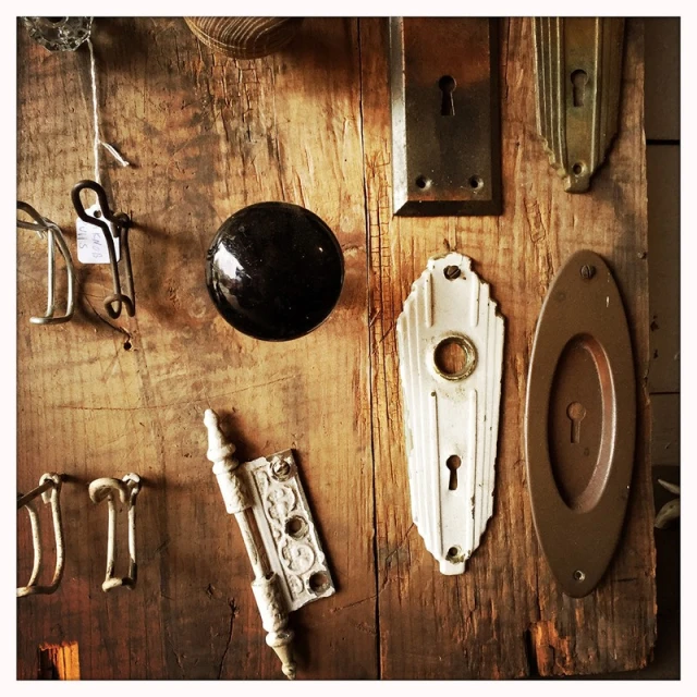 Various antique door hardware including knobs, plates, hinges arranged on a weathered wooden surface.