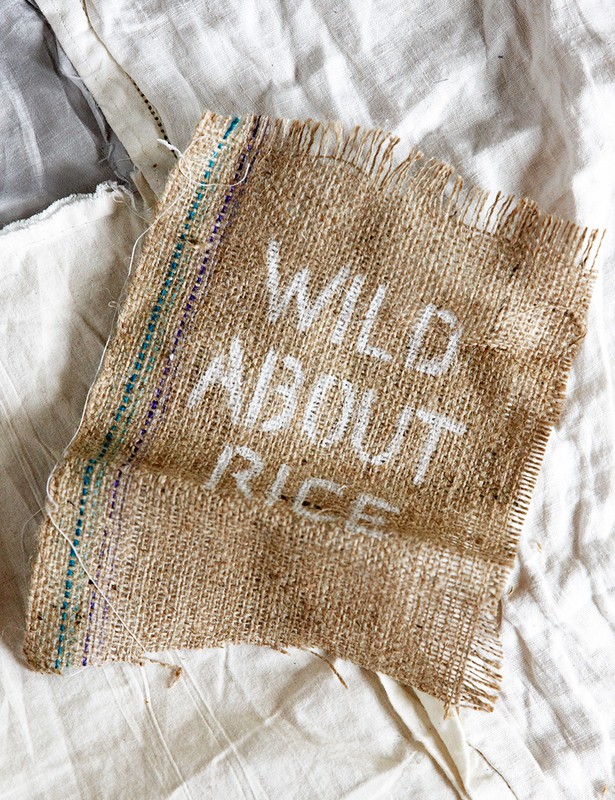 Burlap sack fragment with white lettering 'Wild About Rice' displayed on rumpled white fabric, top-down angle, natural light.