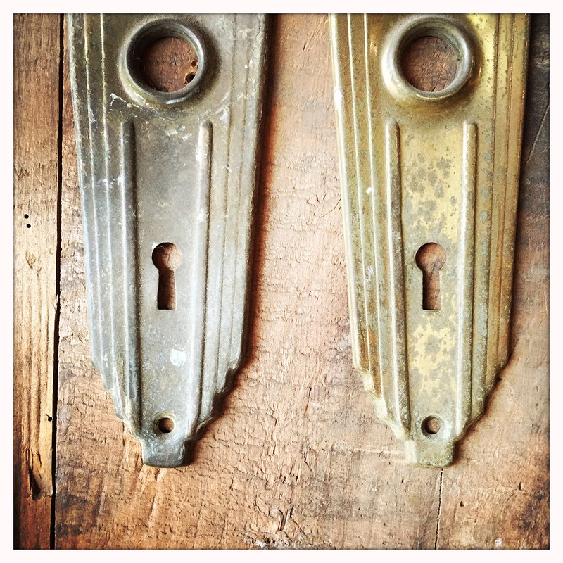 Close-up of two vintage metal doorplates with keyholes mounted on a weathered wood surface, showcasing their aged texture and design.