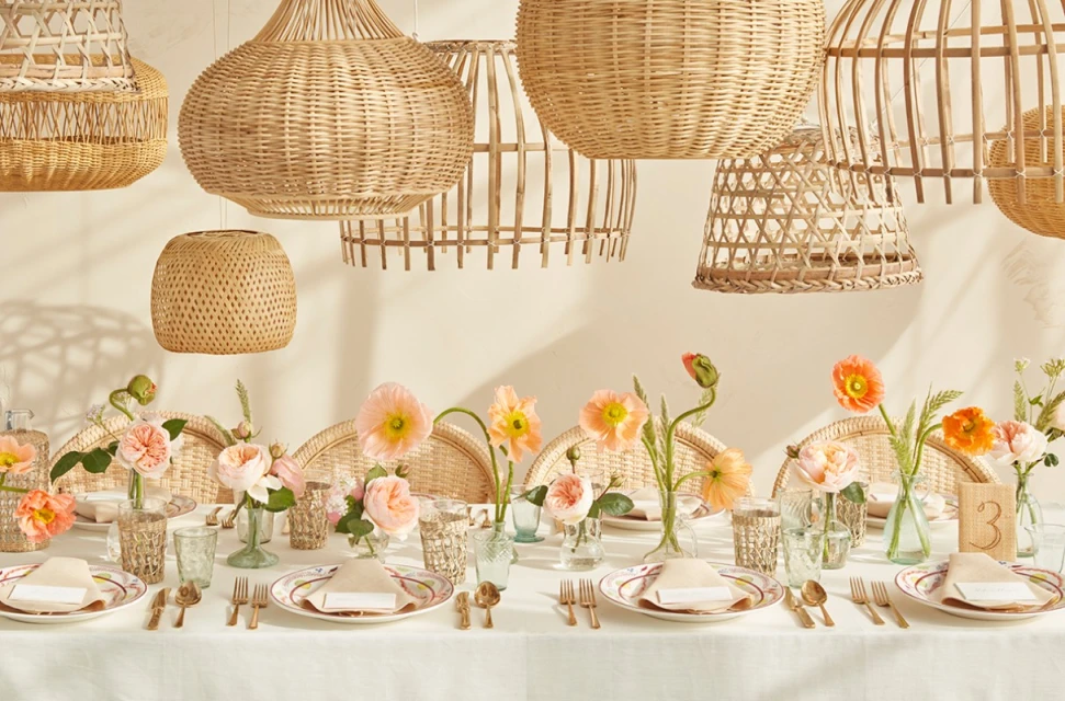 Table setting with flowers, tableware, and woven pendant lights, creating a warm, inviting ambiance for a special occasion.