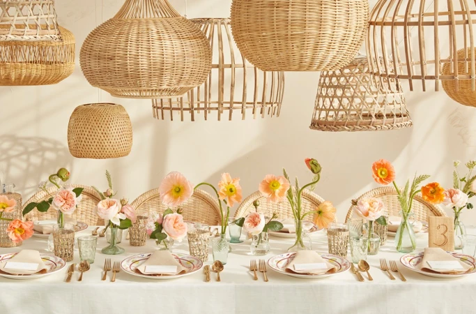 Table setting with flowers, tableware, and woven pendant lights, creating a warm, inviting ambiance for a special occasion.