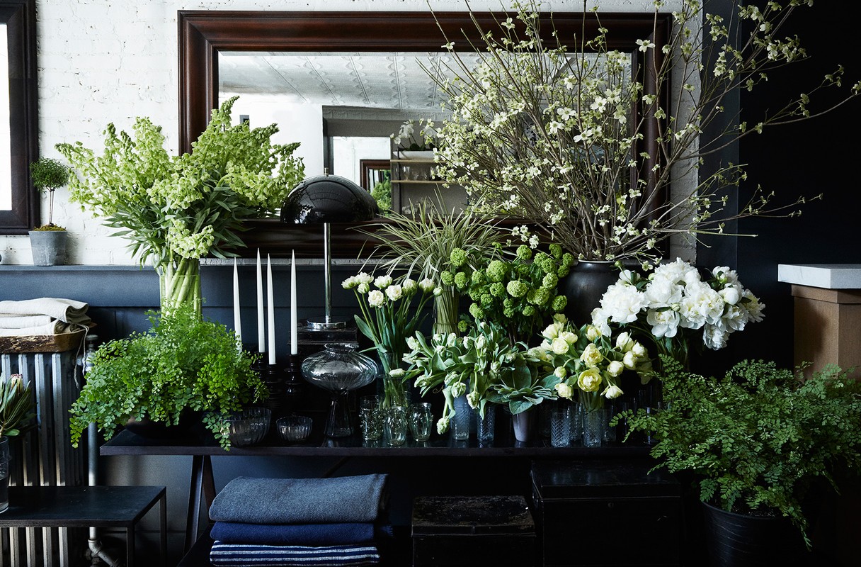 Lush floral arrangements with green and white flowers displayed on a black shelving unit against a white and black wall.