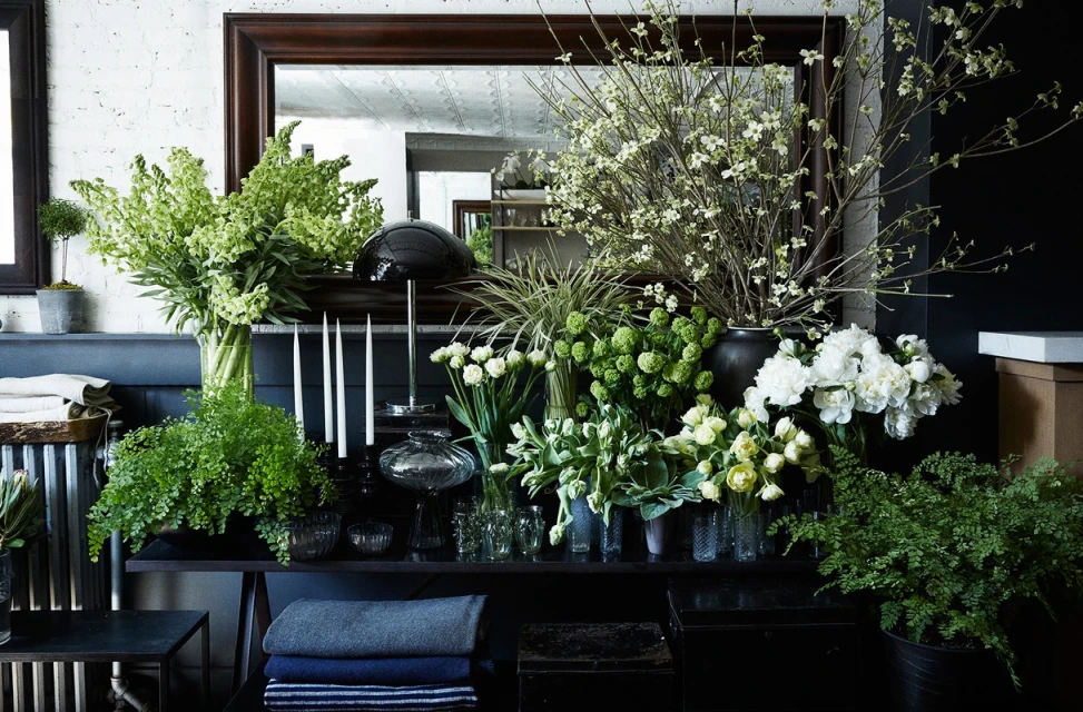 Lush floral arrangements with green and white flowers displayed on a black shelving unit against a white and black wall.