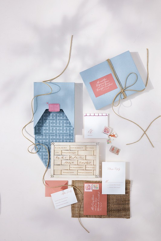 Elevated shot displays a light blue invitation box, stationery, envelopes, stamps, and twine, complemented by natural light and shadows.