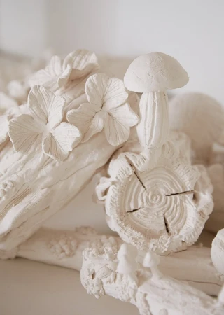 Close-up of white ceramic sculpture featuring botanical details, flowers, and mushroom forms by Pernille Loof.