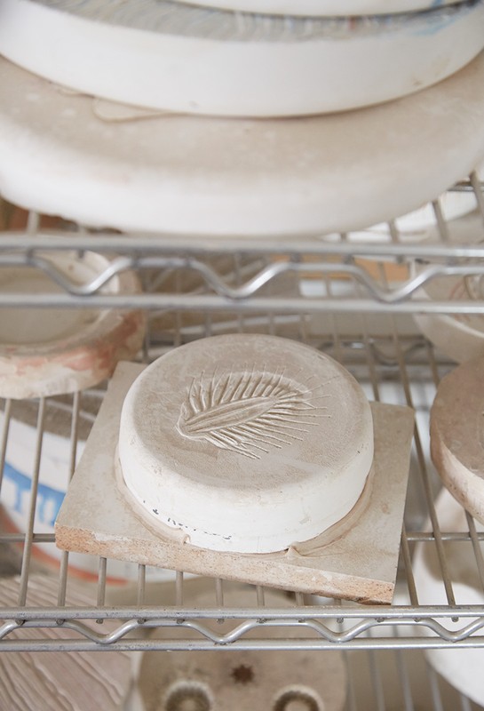Close-up of round, white plaster molds with leaf imprints on a metal shelf, capturing texture, pattern, and craftsmanship.