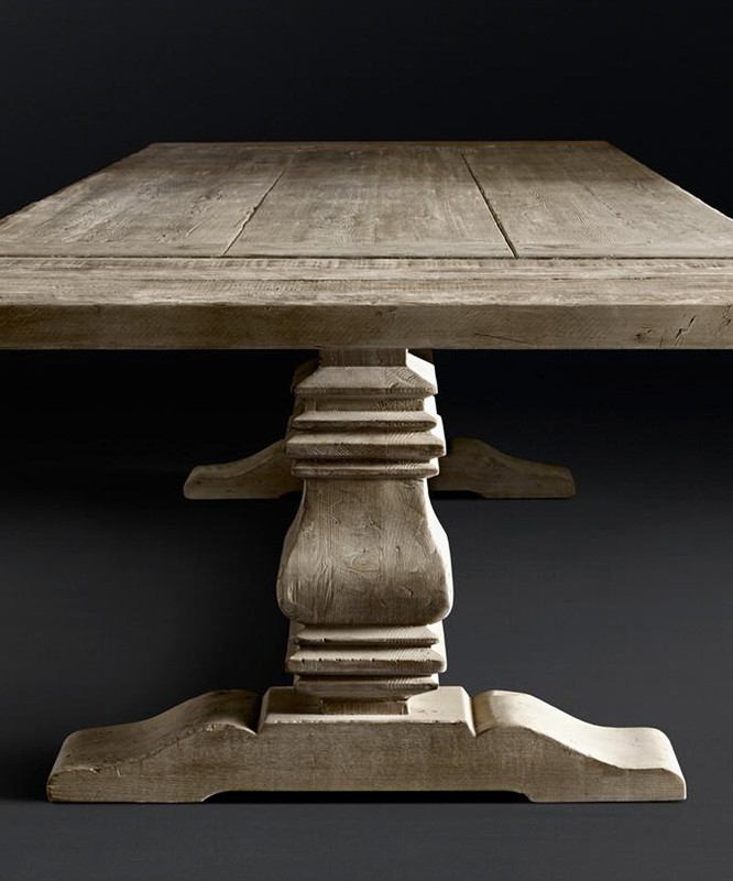 Close-up of a sturdy, square wooden table with a decorative pedestal base, showcasing rustic textures and neutral color palette against dark backdrop.