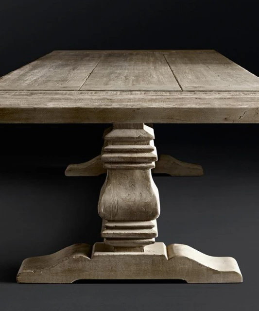 Close-up of a sturdy, square wooden table with a decorative pedestal base, showcasing rustic textures and neutral color palette against dark backdrop.