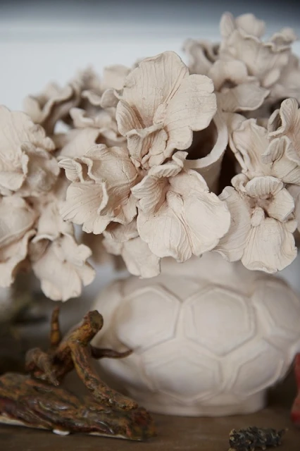 A close-up of a decorative vase filled with textured, abstract floral arrangements in soft, muted earth tones, set indoors.