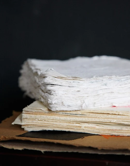 A stack of textured white and beige paper sits against a dark background, highlighting the edges and tactile qualities.