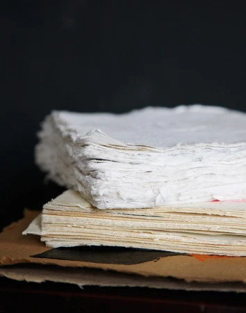 A stack of textured white and beige paper sits against a dark background, highlighting the edges and tactile qualities.