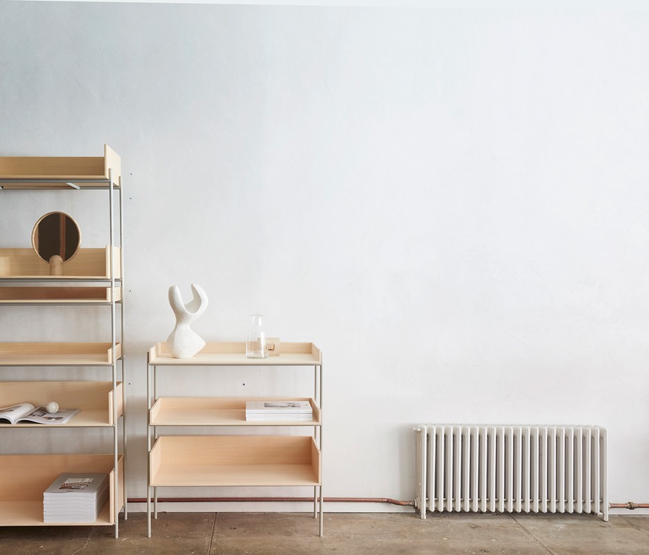 Minimalist interior with wooden shelving units displaying a vase, mirror, books, and a water carafe against a white wall.