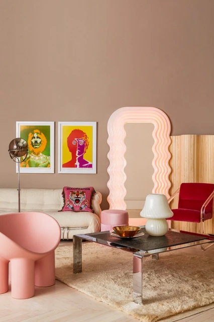 Interior design with pink and red armchairs, artwork of portraits, lamp, and coffee table on a shag rug in a monochrome room.