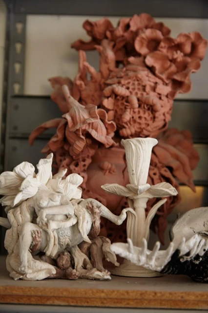 Still life of a collection of clay sculptures featuring floral and figure themes, displayed on a shelf indoors, bathed in soft lighting.