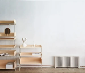Minimalist interior with wooden shelving units, a white ceramic sculpture, books, and a radiator against a plain wall