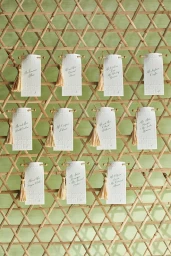 Hanging place cards with calligraphy and tassels arranged on a wooden lattice wall by photographer Pernille Loof.