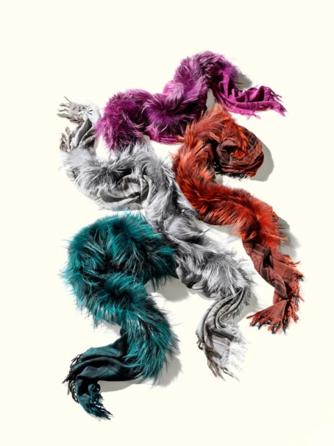 Four colorful scarves with fur trim, each with a distinct hue – purple, orange-red, gray, and teal – arranged on a pale background.