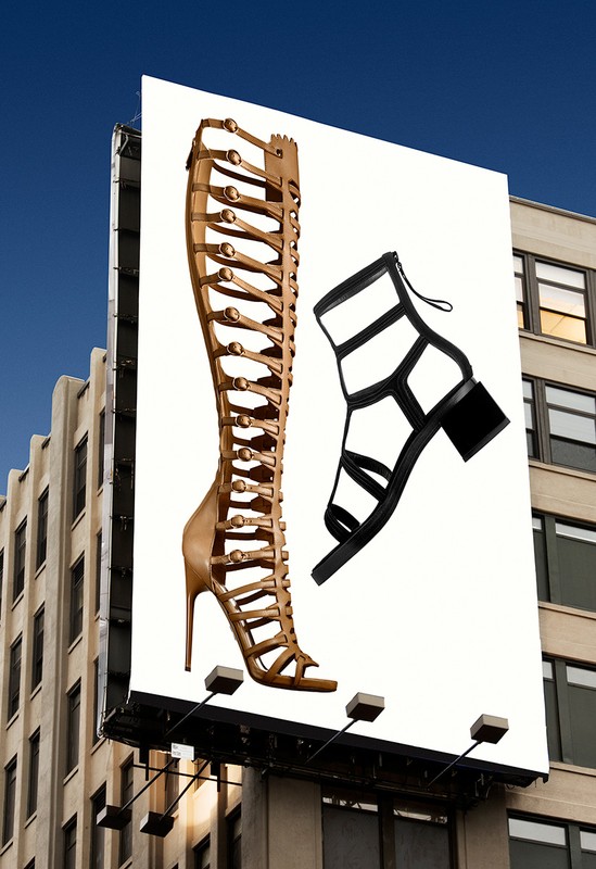 Billboard featuring a tall strappy sandal and a cage sandal against a clear blue sky and the side of a tan building.