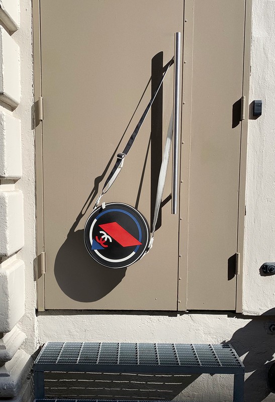 Round Chanel handbag hangs on a metal door handle outside on a sunny day, showcasing luxury fashion and urban aesthetics.