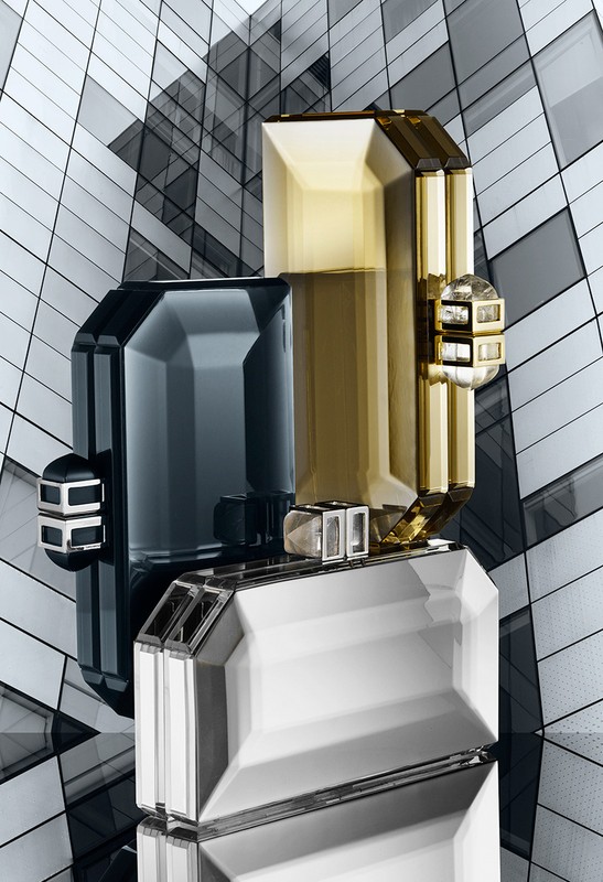 Still life of three rectangular crystal clutch purses in silver, gold, and dark grey against an abstract geometric background.