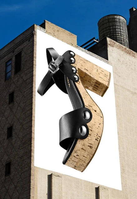 Advertisement featuring a platform sandal with a black leather upper and cork heel, displayed on the side of a building with a blue sky.