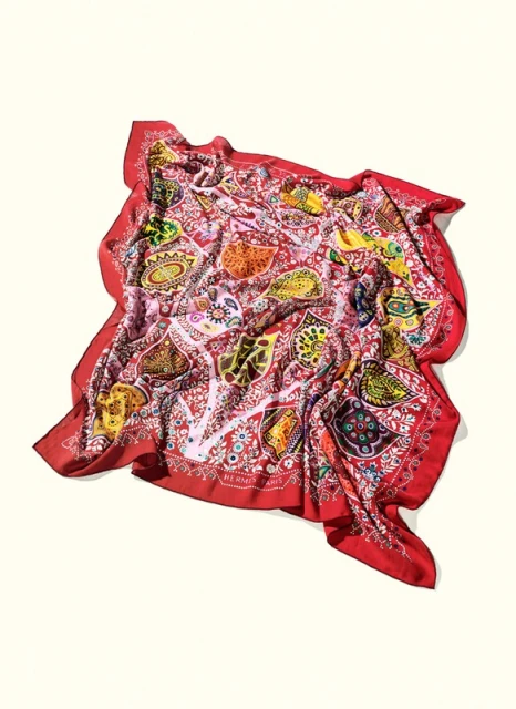 Overhead studio shot of a vibrant, patterned red scarf with paisley-like designs, elegantly draped against a clean, neutral background.