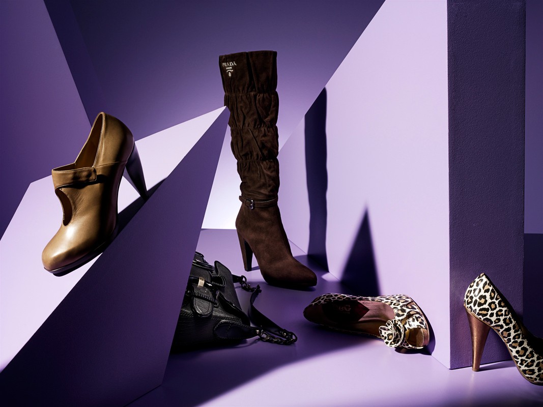 Fashion still life showcasing a brown Prada boot, beige heeled pump, leopard print heels, and a black purse against a geometric purple backdrop.