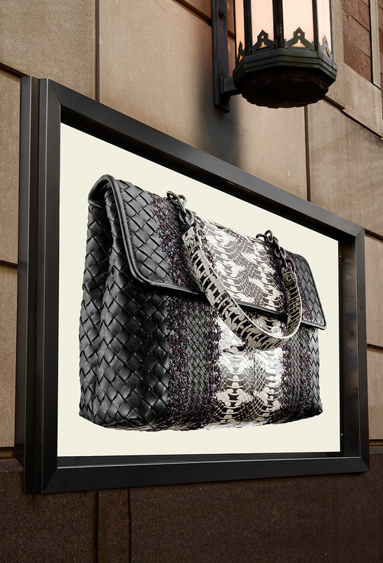 Fashion handbag display with black woven leather and white snake skin design mounted on an exterior building wall next to a light fixture.