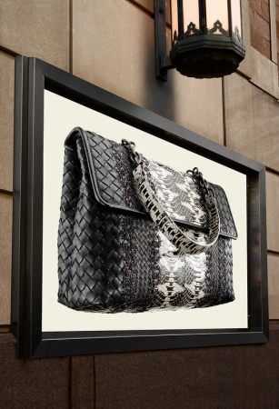 Fashion handbag display with black woven leather and white snake skin design mounted on an exterior building wall next to a light fixture.