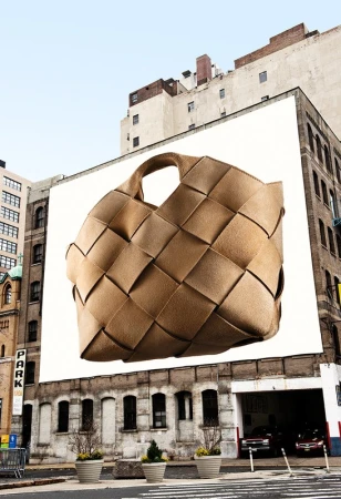 Large woven tan leather handbag floating against a white billboard on an urban building exterior in Los Angeles.