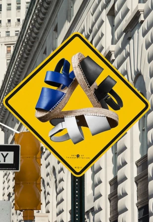 Fashion-forward product shot of blue, white, and black strappy sandals arranged atop a yellow street sign, set against a building exterior.