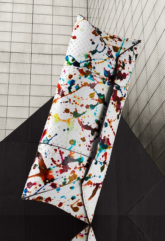 Abstract still life of a white clutch purse with colorful paint splatter on a black and white geometric background.