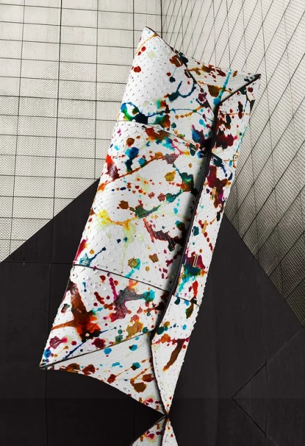 Abstract still life of a white clutch purse with colorful paint splatter on a black and white geometric background.