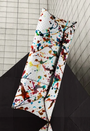 Abstract still life of a white clutch purse with colorful paint splatter on a black and white geometric background.