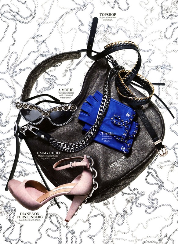 Fashion flat lay featuring a black purse, pink heels, blue gloves, sunglasses, and a black belt, all accented with silver chains.