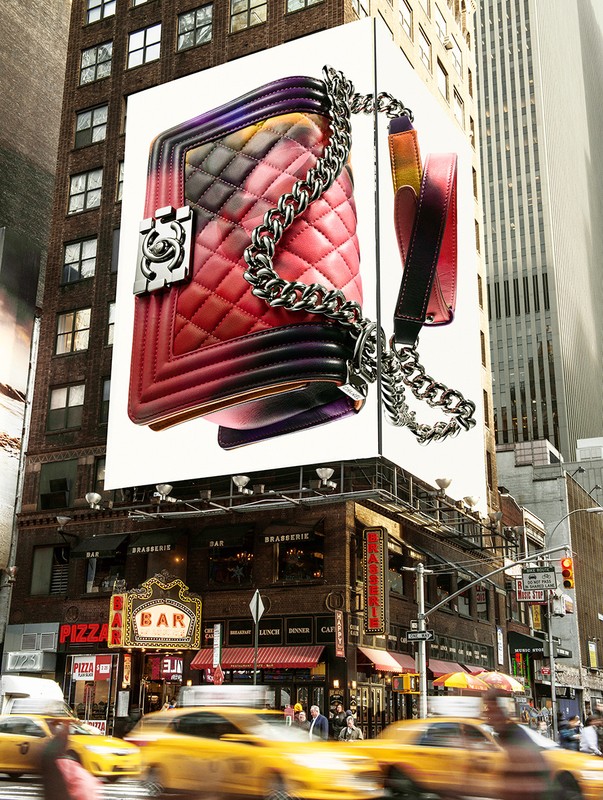 Fashion billboard in a cityscape featuring a red gradient quilted handbag with a silver chain strap on a modern urban building.