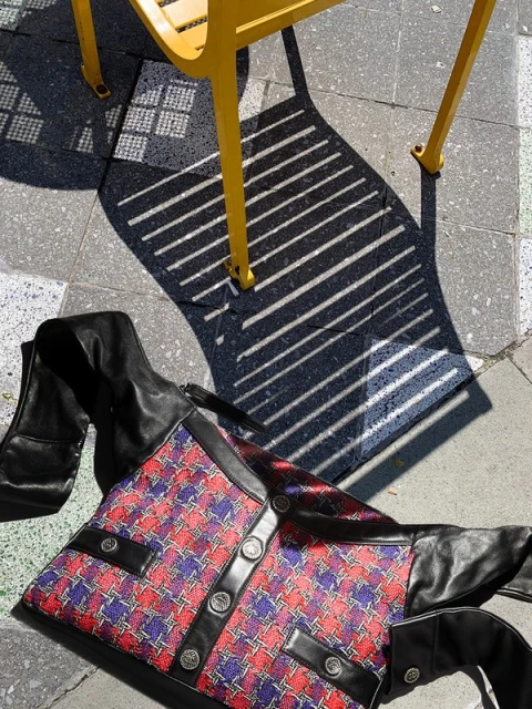 A red and blue patterned jacket lies on a gray stone surface with the shadow of a yellow chair, under bright light, creating strong contrast.