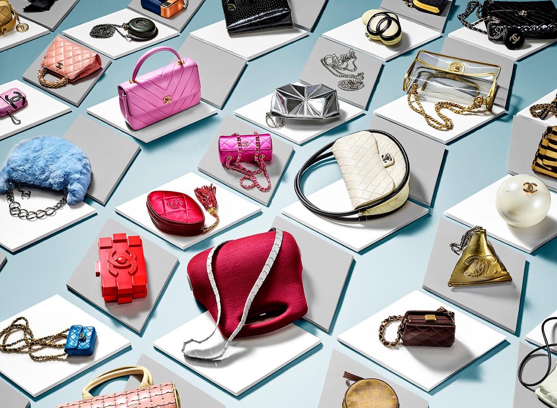 High-angle shot of assorted colorful Chanel handbags arranged on white platforms against a blue background in a studio setting.