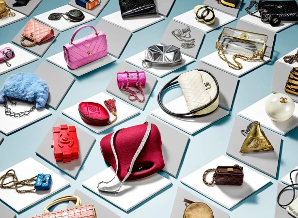 An overhead arrangement of various luxury designer handbags displayed on angled white and grey pedestals against a light blue background.