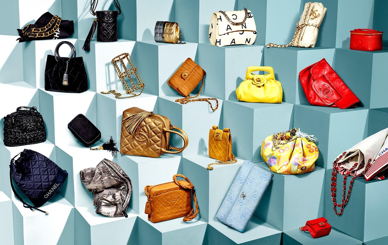 Display of assorted Chanel handbags in various colors and styles arranged on tiered blue cube platforms, well-lit and detailed.