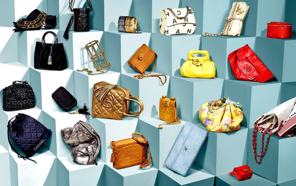 Display of assorted Chanel handbags in various colors and styles arranged on tiered blue cube platforms, well-lit and detailed.